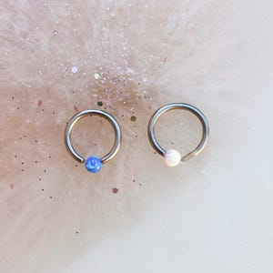 May include: Two silver hoop earrings with a small blue opal gemstone and a white opal gemstone.
