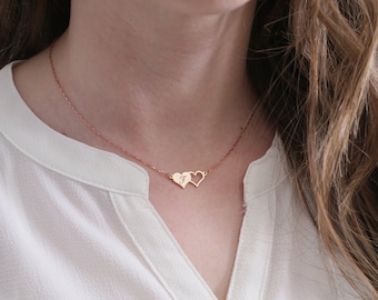 May include: A delicate gold necklace with two interlocking heart pendants. The necklace is worn by a person with long brown hair.