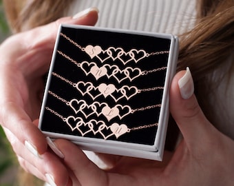 May include: A white box with a black interior containing a set of rose gold heart-shaped bracelets with initial charms. Each bracelet has a different initial charm.