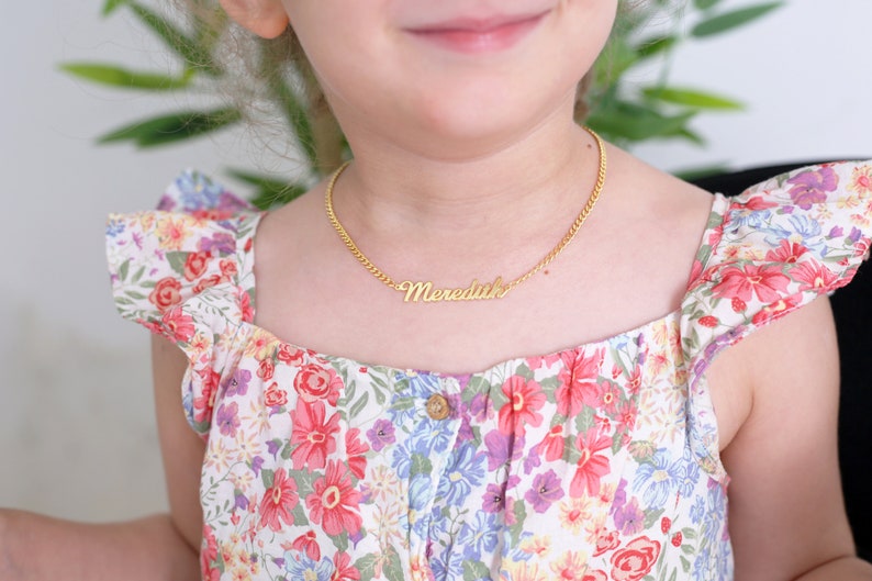 Pu&ograve; includere: Una giovane persona che indossa un vestito bianco con un motivo floreale e una collana d'oro con il nome "Meredith" su di essa.
