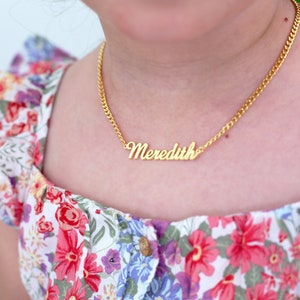 Pu&ograve; includere: Una collana a catena dorata con un ciondolo a placca con il nome "Meredith".