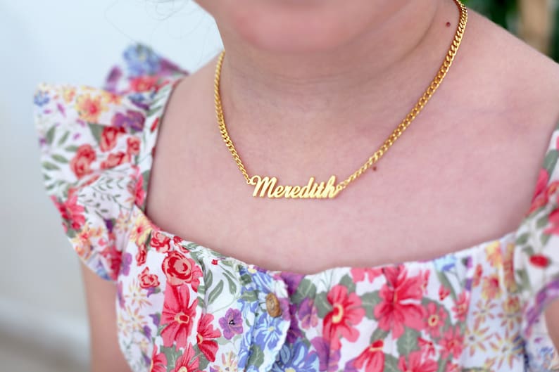 Pu&ograve; includere: Una collana a catena dorata con un ciondolo a placca con il nome "Meredith".