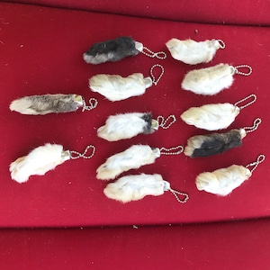 May include: Twelve furry rabbit foot keychains with silver rings and chains. The keychains are arranged in two rows on a red surface.