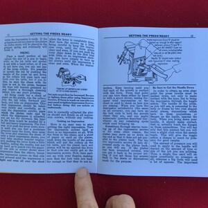 May include: A close-up of a page from a book titled "Getting the Press Ready." The page shows a diagram of a printing press with instructions on how to adjust the impression screws and handle. The text includes the phrase "Be Sure to Get the Handle Down."