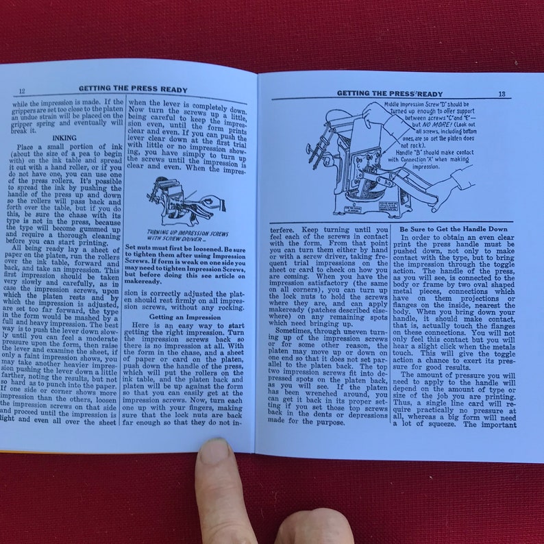May include: A close-up of a page from a book titled "Getting the Press Ready." The page shows a diagram of a printing press with instructions on how to adjust the impression screws and handle. The text includes the phrase "Be Sure to Get the Handle Down."