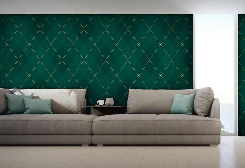 Op de afbeelding: Een grote, grijze hoekbank met twee tealblauwe kussens staat voor een muur met een groene en gouden diamantpatroon behang.