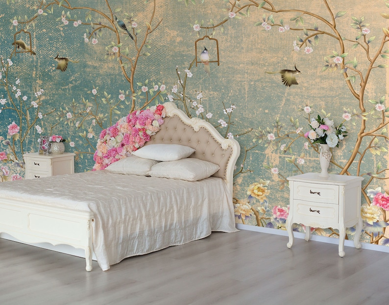 May include: A white bed frame with a white headboard and a white bedspread. The headboard is decorated with a floral design. The bed is in a room with a floral wallpaper and two white nightstands.