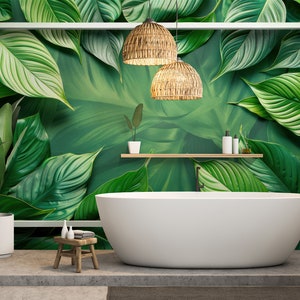 Op de afbeelding: Een wit bad staat in een badkamer met een tropische bladbehang. Twee geweven hanglampen hangen boven het bad. Een kleine houten kruk met een opgerolde handdoek staat naast het bad.