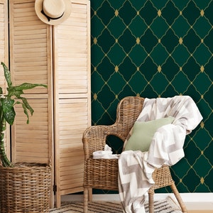 May include: A wicker chair with a white and gray throw blanket and a green pillow sits in front of a green and gold geometric wallpaper.