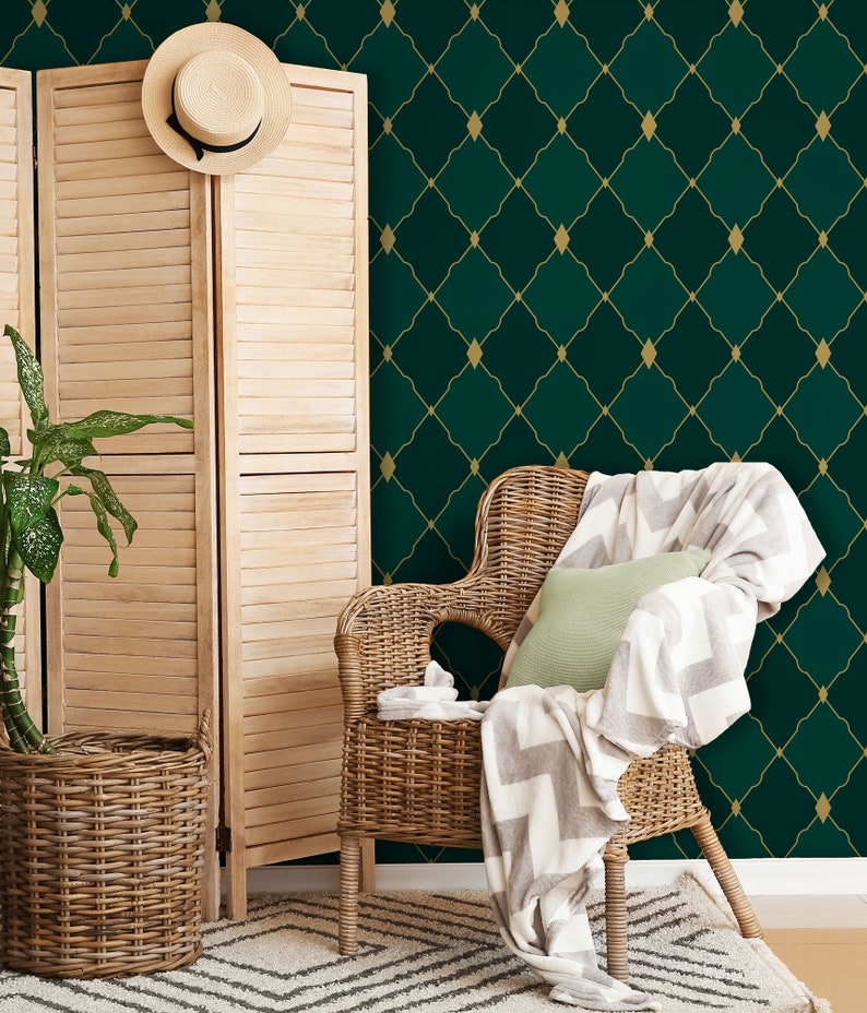 May include: A wicker chair with a white and gray throw blanket and a green pillow sits in front of a green and gold geometric wallpaper.