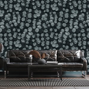 Puede incluir: Un sofá de cuero negro con un papel tapiz estampado en gris oscuro con hojas blancas. El sofá está frente a una pared azul verdosa y una alfombra gris oscuro.