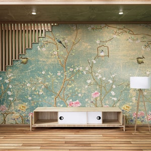 May include: A wooden TV stand with two drawers and a floral wallpaper with birds behind it. The stand is in a room with a wooden floor and green walls.
