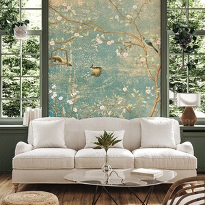 May include: A white sofa with two pillows and a green plant on a glass coffee table in front of a wall with a floral wallpaper design.