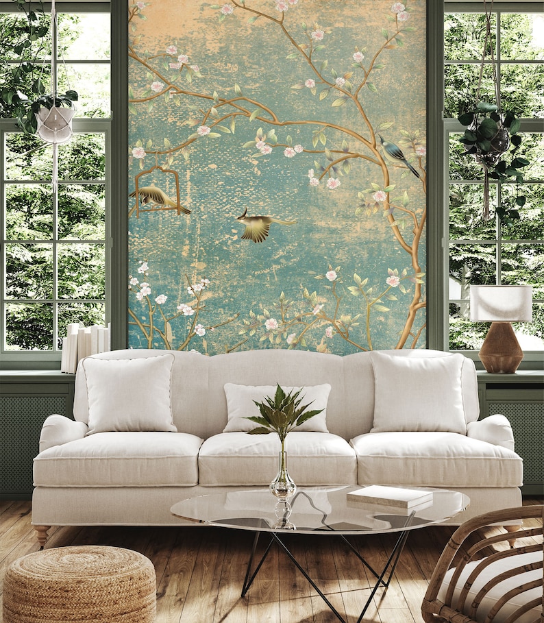 May include: A white sofa with two pillows and a green plant on a glass coffee table in front of a wall with a floral wallpaper design.