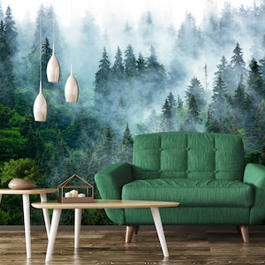 Puede incluir: Un sofá verde con un papel tapiz de escena de bosque detrás. El papel tapiz presenta un bosque brumoso con árboles verdes altos. Hay tres luces colgantes plateadas que cuelgan del techo.
