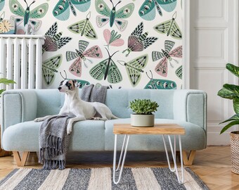 May include: A light blue sofa with a gray throw blanket and a dog sitting on it. The wall behind the sofa has a wallpaper with a pattern of green and pink butterflies.