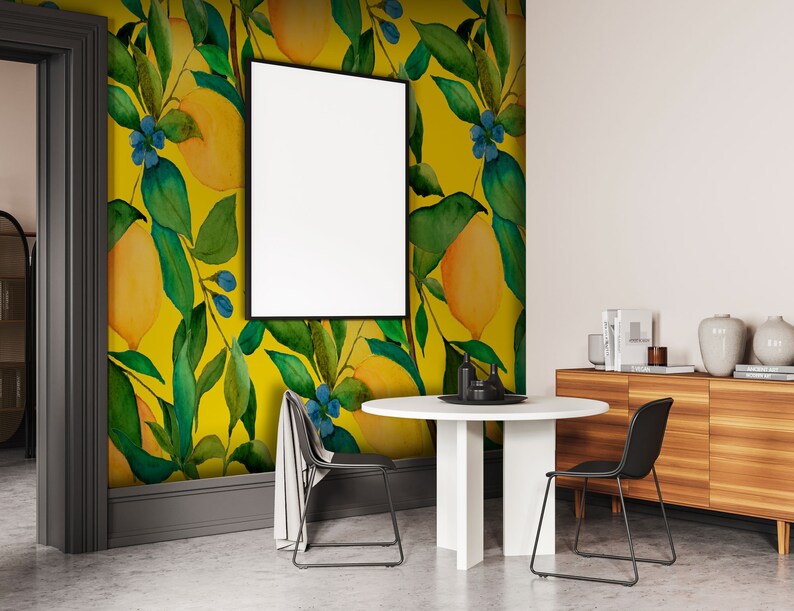 Puede incluir: Un comedor con papel tapiz amarillo y verde con motivos de limones, una mesa redonda blanca con dos sillas negras y un aparador de madera con libros y objetos decorativos.