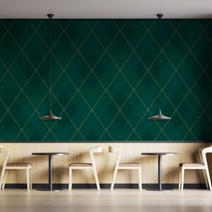Op de afbeelding: Een groene en gouden gepatroneerde muur met drie zwarte hanglampen die boven een rij van drie houten stoelen en tafels hangen. De stoelen en tafels zijn symmetrisch gerangschikt.