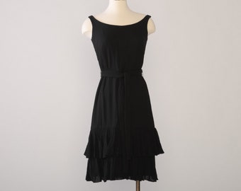 May include: A black sleeveless dress with a ruffled hem and a matching belt. The dress is on a white mannequin.
