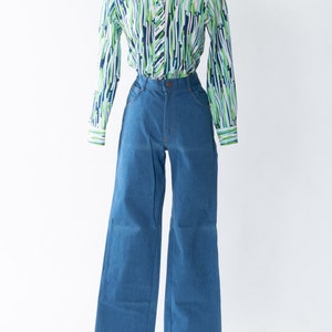 May include: A blue and green striped long-sleeved shirt with a collared neckline and button closure. The shirt is paired with blue denim wide-leg pants.