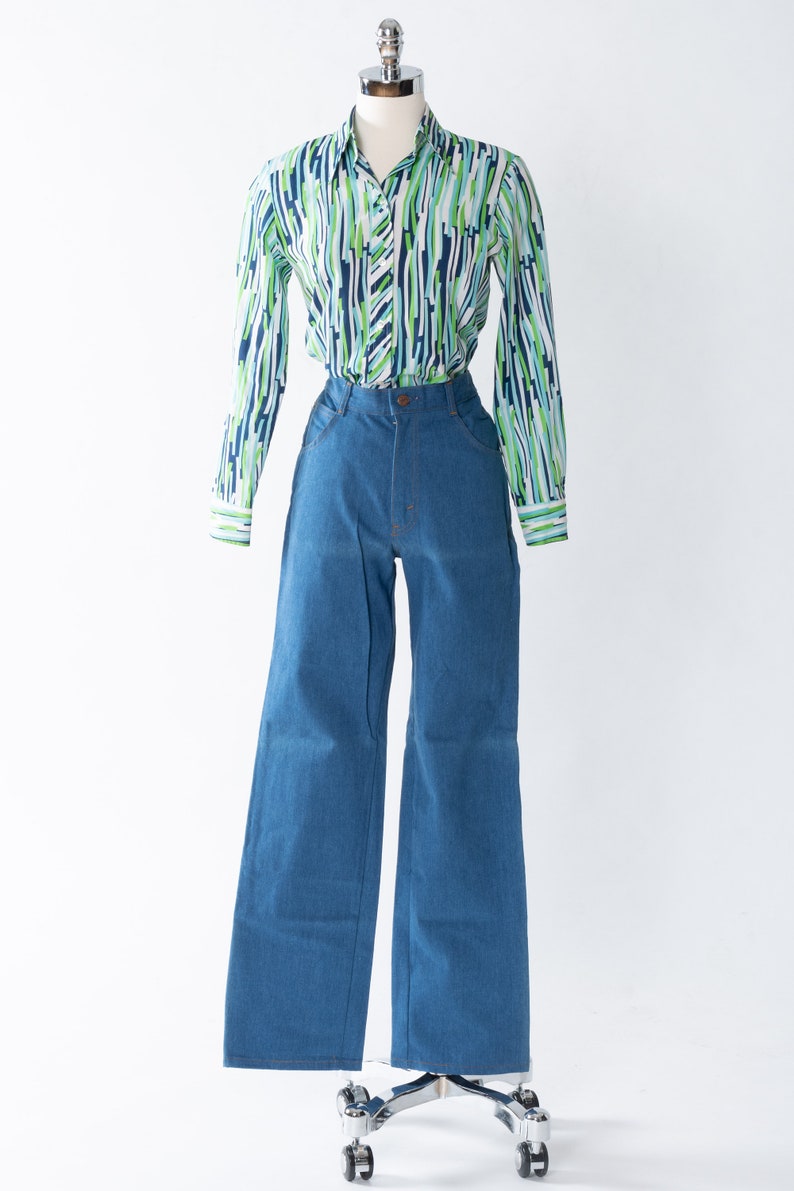 May include: A blue and green striped long-sleeved shirt with a collared neckline and button closure. The shirt is paired with blue denim wide-leg pants.