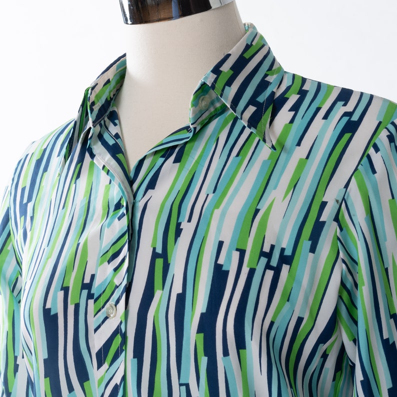 May include: A white button-down shirt with a blue, green, and white abstract pattern. The shirt has a long sleeve and a collar.