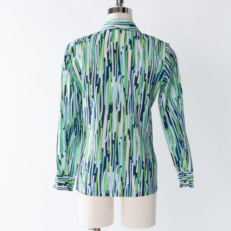 May include: A white long-sleeved shirt with a blue, green, and white abstract pattern. The shirt has a button-up collar and long sleeves with button cuffs.