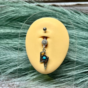 May include: Silver belly button ring with a turquoise and black dangle charm shaped like a lightning bolt.