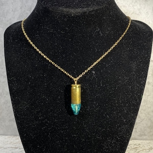 May include: A gold chain necklace with a bullet pendant filled with blue resin.