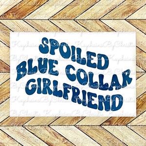 May include: A white rectangular sign with the text "SPOILED BLUE COLLAR GIRLFRIEND" in dark blue, bubble-style letters. The sign is set against a wooden chevron pattern background.