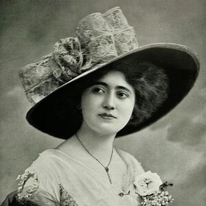 May include: A vintage black and white portrait of a woman wearing a large, wide-brimmed hat. The hat features a prominent lace bow and a dark brim. She is also wearing a light-colored dress and a delicate necklace. A white rose is pinned to her dress.
