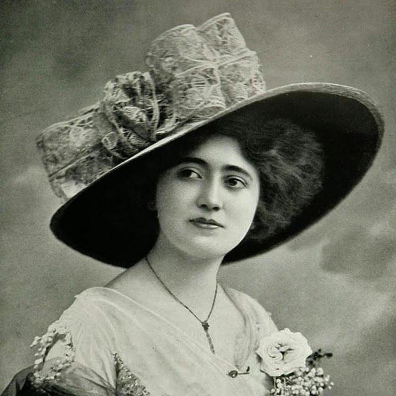 May include: A vintage black and white portrait of a woman wearing a large, wide-brimmed hat. The hat features a prominent lace bow and a dark brim. She is also wearing a light-colored dress and a delicate necklace. A white rose is pinned to her dress.
