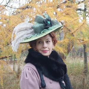 May include: A light green hat with a wide brim, adorned with a large green bow, black embellishments, and white feathers. The hat is worn with a pink coat and a black fur stole.