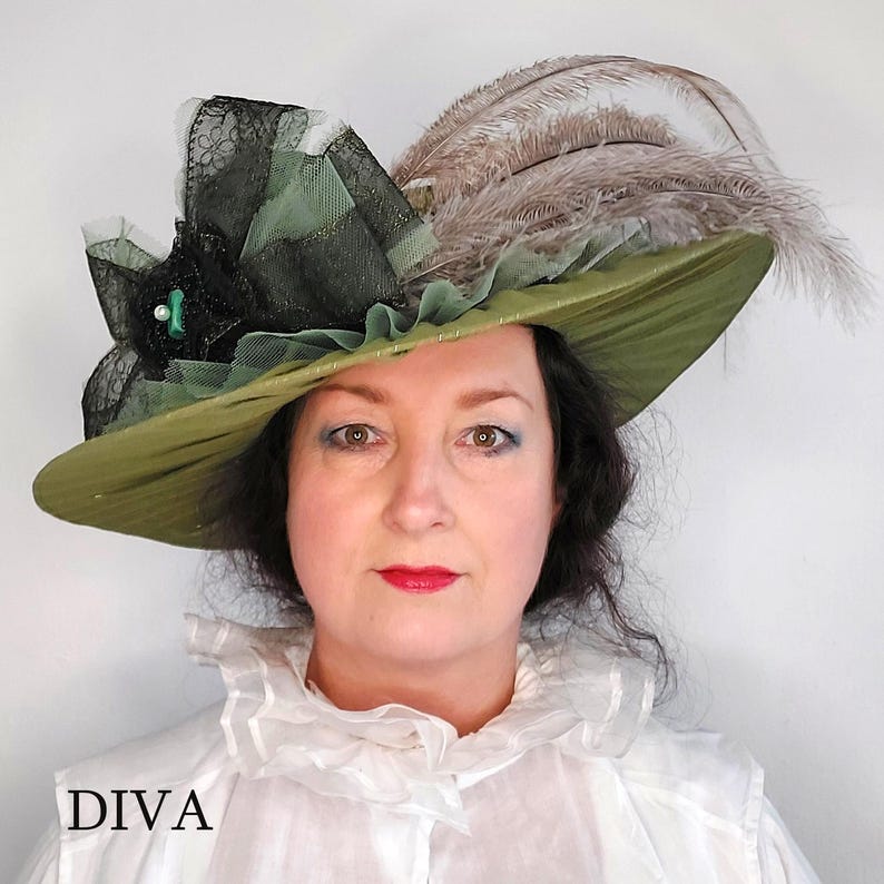 May include: An olive green hat with a wide brim, adorned with black lace, green fabric, and brown feathers. A black flower with a pearl and a green gem is on the side. The word "DIVA" is printed at the bottom.