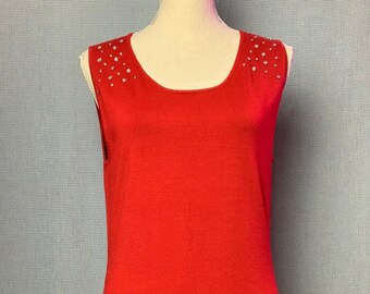 May include: A sleeveless red knit top featuring a scoop neckline and a series of small, clear, reflective rhinestones scattered across the shoulder areas. The garment has a straight hemline and a smooth, solid-colored fabric construction.