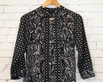May include: A black and white long-sleeve tunic featuring a mandarin collar and a button-down front. The garment displays a contrasting pattern with a dense floral-like print on the body and a geometric star-like motif on the sleeves and placket.
