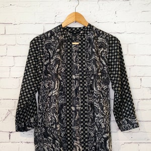 May include: A black and white long-sleeve tunic featuring a mandarin collar and a button-down front. The garment displays a contrasting pattern with a dense floral-like print on the body and a geometric star-like motif on the sleeves and placket.