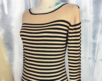 May include: A long-sleeved, ribbed knit sweater featuring a horizontal striped pattern in black and beige. The garment has a wide, rounded boat neckline with a solid beige yoke at the top and a fitted silhouette that extends down to the waist.