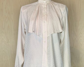 Op de afbeelding: Een lichtroze blouse met lange mouwen, een hoge opstaande kraag, een knoopsluiting aan de voorzijde en een groot, gedrapeerd ruchepaneel over de borst. De stof is voorzien van een subtiel, tonaal jacquardpatroon over het gehele kledingstuk.