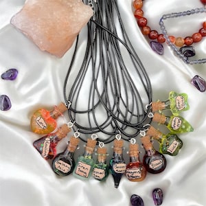 May include: A set of ten glass bottle necklaces with cork stoppers. Each bottle contains colourful liquid and glitter. The bottles have labels with different names, including "Love", "Healing", "Galaxy Mix", "Siren Song", "Bottled Storm", "Dragons Breath", "Blood", "Luck", "Specky", and "Star Juice".