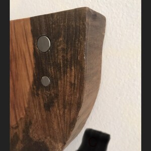 May include: Close-up of a wooden wall shelf with a natural wood finish. The shelf has a curved edge and is attached to the wall with two silver metal screws.
