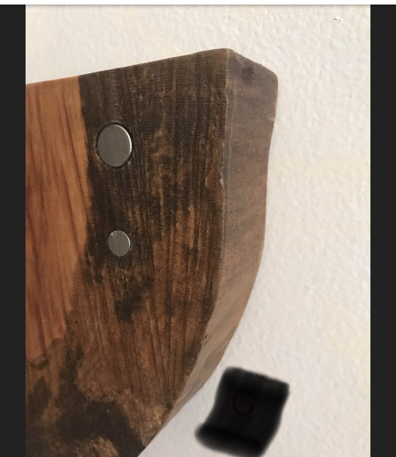 May include: Close-up of a wooden wall shelf with a natural wood finish. The shelf has a curved edge and is attached to the wall with two silver metal screws.