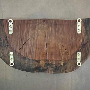 May include: A large, dark wood slice with a natural edge, featuring a unique grain pattern. It has four brass hanging brackets attached to the back. The wood slice is signed "Below 74" and "3116F4".