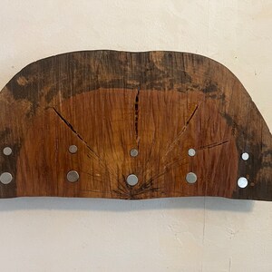 May include: A wooden half-circle with a natural wood grain and a dark brown stain. The wood has a radial pattern with several cracks. There are eight silver metal discs attached to the wood.