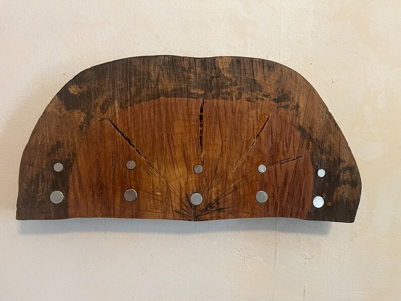 May include: A wooden half-circle with a natural wood grain and a dark brown stain. The wood has a radial pattern with several cracks. There are eight silver metal discs attached to the wood.