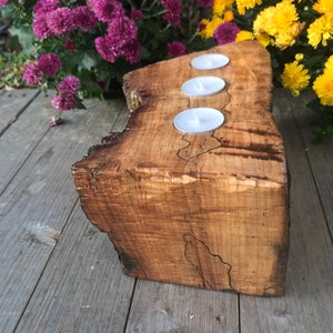 May include: A wooden candle holder with three candle wells. The holder is made from a natural wood slice with a rustic finish.