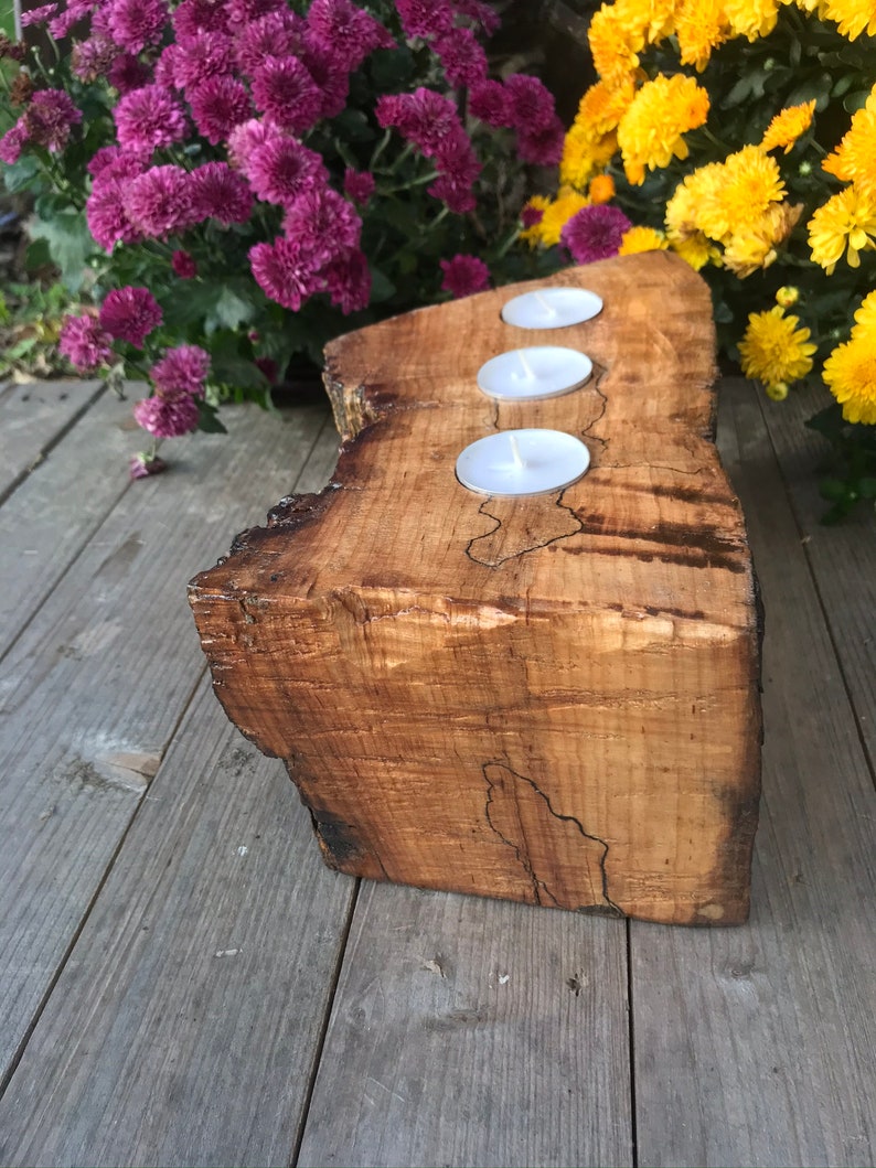 May include: A wooden candle holder with three candle wells. The holder is made from a natural wood slice with a rustic finish.