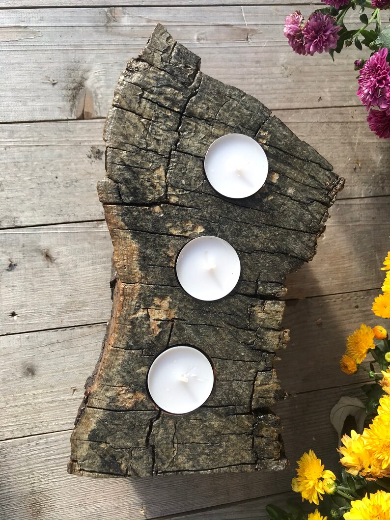 May include: A rustic wooden candle holder with three white tea lights. The holder is made from a natural piece of wood with a rough, textured surface.