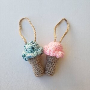 Peut inclure: Deux ornements en forme de cornet de cr&egrave;me glac&eacute;e en crochet avec des boucles de ficelle marron. Un cornet de cr&egrave;me glac&eacute;e est vert et l'autre est rose.