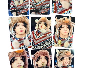 May include: A collection of nine rectangular photo cards featuring a person wearing a brown plush cow-themed hat with horns and dangling pom-poms, paired with a colorful patterned sweater featuring geometric and animal motifs.